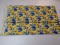 Floral fabric with blue flowers on a yellow background, folded and displayed on a white surface.