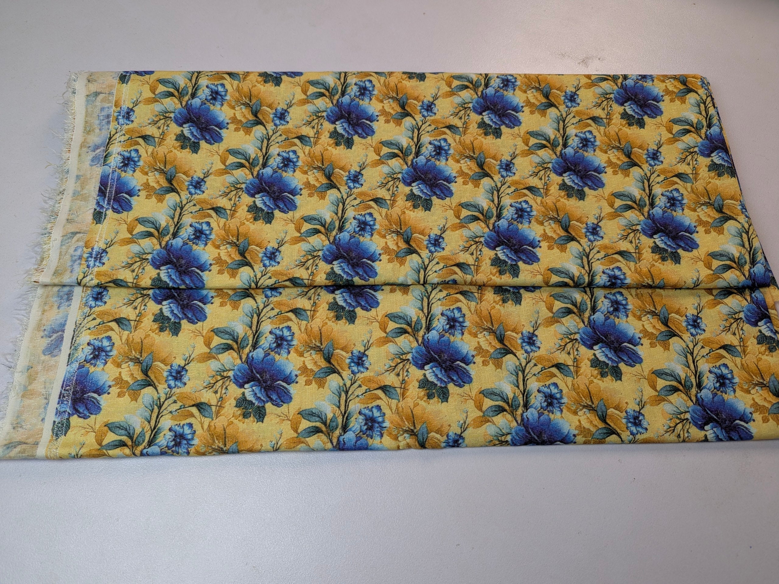 Floral fabric with blue flowers on a yellow background, folded and displayed on a white surface.