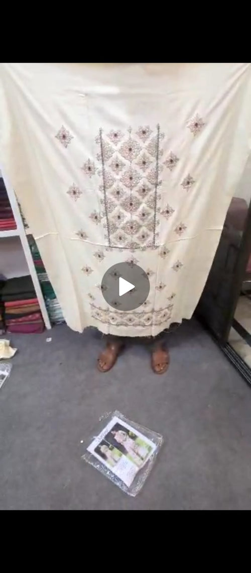 Person wearing a cream-colored traditional outfit with intricate patterns, standing in a room.
